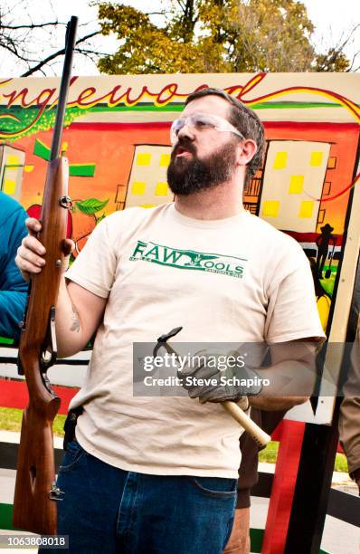 View of American religious activist and blacksmith Michael Martin, of the RAWTools organization, as he holds a rifle in hand and a garden tool in the...
