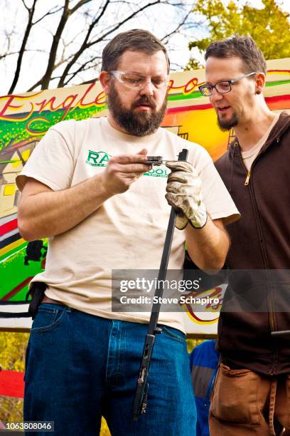 Low-angle view of American religious activist and blacksmith Michael Martin, of the RAWTools organization, as he holds a rifle barrel and takes a...