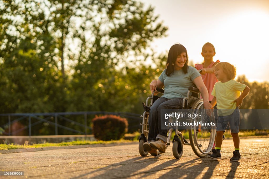 Mujeres jóvenes en silla de ruedas paseando con los niños al atardecer
