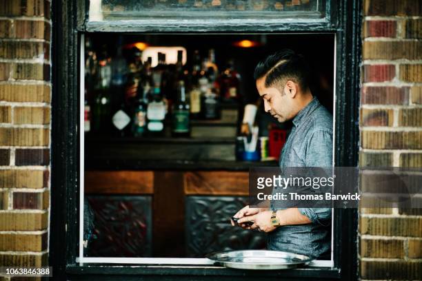 View through window of bartender checking smart phone