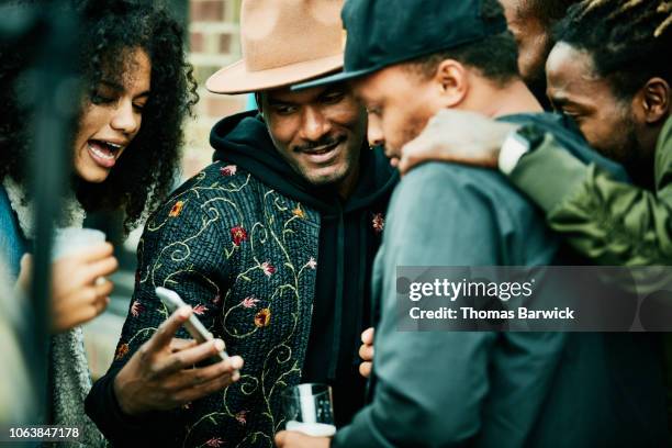 friends looking at smart phone during party at outdoor restaurant - male friendship stock pictures, royalty-free photos & images