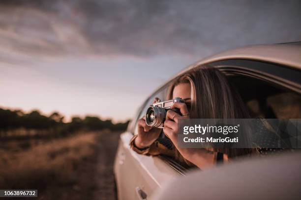 young woman taking a picture with a vintage camera from car window - car photo shoot stock pictures, royalty-free photos & images