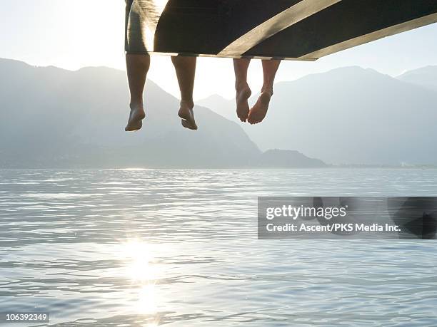 couple's feet dangle from end of lake wharf - bergsteiger stockfoto's en -beelden