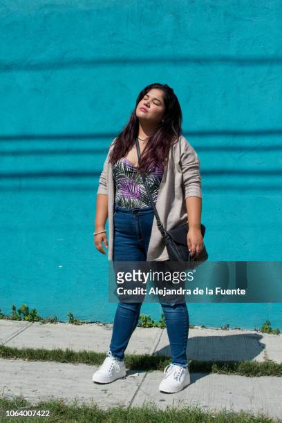 portrait of a beautiful latina woman standing in front of a blue wall. - blue purse stock pictures, royalty-free photos & images