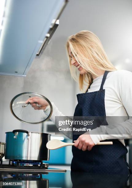 mooie blonde vrouw in haar keuken koken controleert vooruitgang, lachende - deksel stockfoto's en -beelden