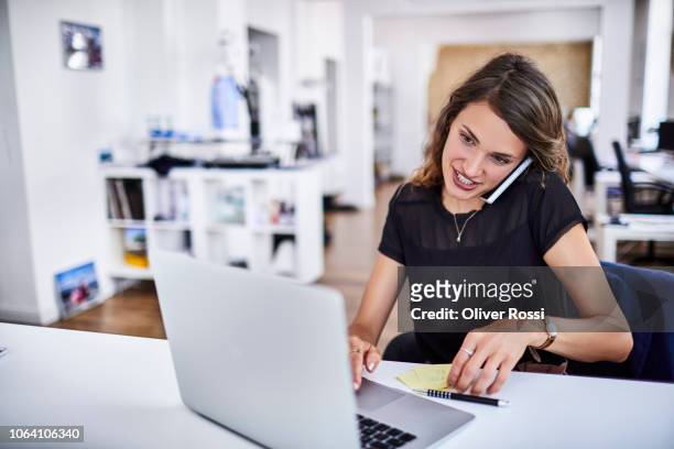 young businesswoman using laptop and cell phone in office - busy woman stock-fotos und bilder
