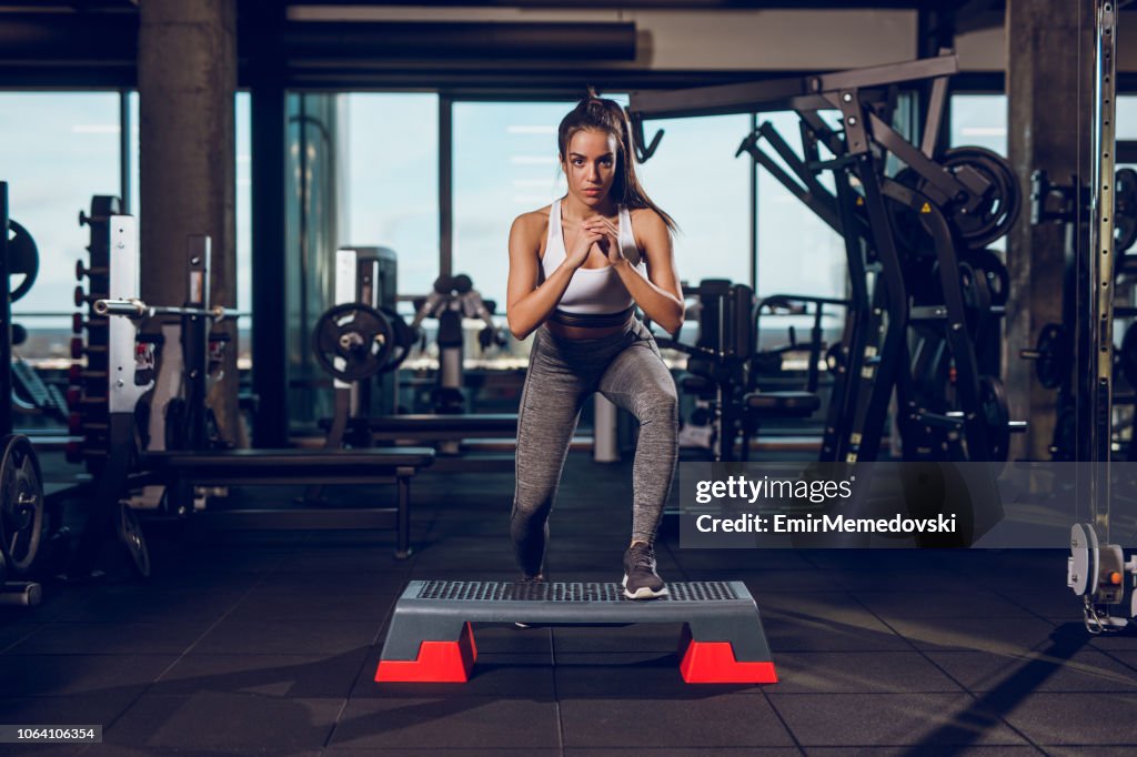 Giovane donna che si allena con attrezzatura aerobica a gradini in palestra