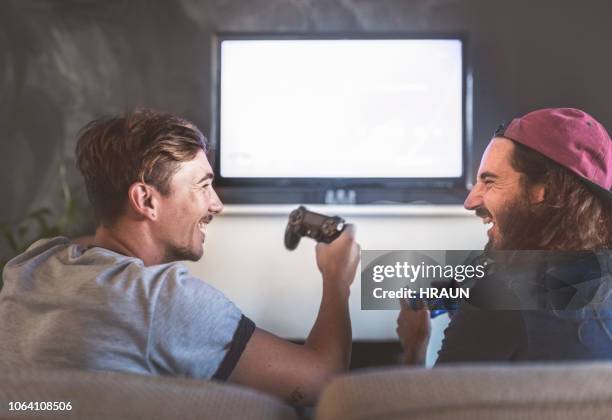 cheerful young men playing video game at home - back of sofa stock pictures, royalty-free photos & images