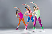 attractive sporty girls in bodysuits training at aerobics workout on grey