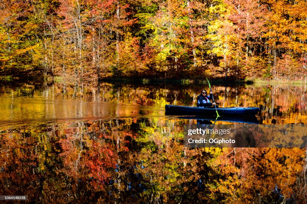 Mujer de kayak en el lago que refleja los colores del otoño