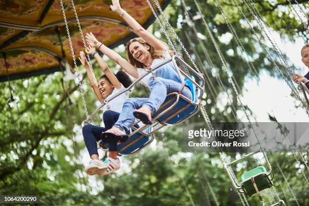 happy mother and daughter in a swing carousel - amusement park stock pictures, royalty-free photos & images