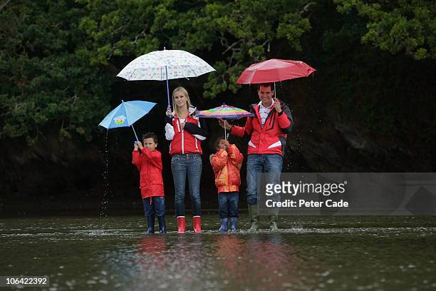 family stood on flooded road in the rain - mother protecting from rain stock-fotos und bilder