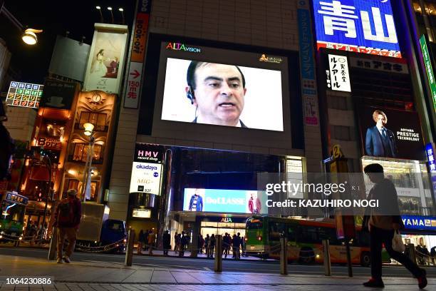 Pedestrian walks past a screen showing a news programme featuring Nissan chairman Carlos Ghosn in Tokyo on November 22, 2018. - Top executives from...