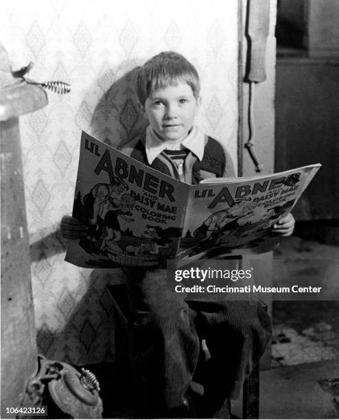 Young boy looks up while reading a Li'l Abner coloring book, Cincinnati, OH, mid to late twentieth century.