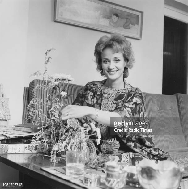 Portrait of actress Sylvia Syms sitting on a sofa and arranging flowers, November 1971.