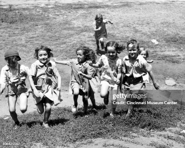 Group of young boys and girls smile and laugh while running up a hill, in one of Cincinnati's inner city neighborhoods, mid to late twentieth century.