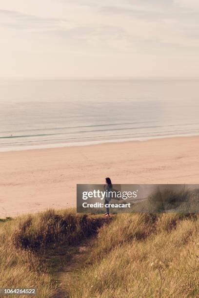 frau mit blick auf gwithian towan strand, cornwall, in der nähe von sonnenuntergang an einem junitag surfbrett. - gwithian stock-fotos und bilder