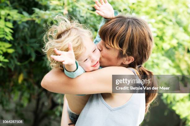mother cuddles and kisses toddler in garden. - bébé rire photos et images de collection