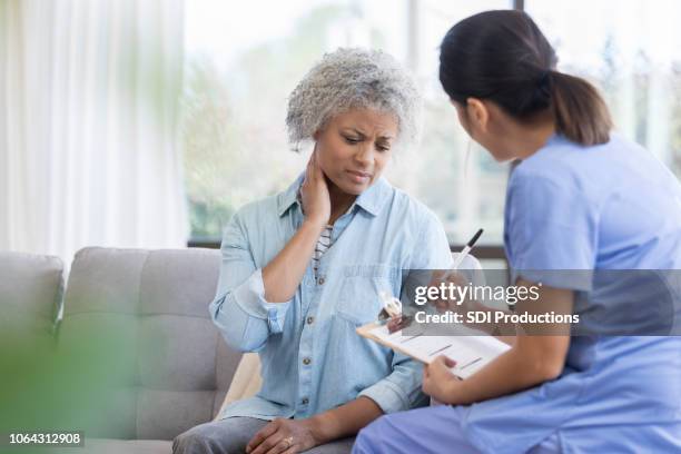 senior woman describes neck pain during doctor's house call - stern form stock pictures, royalty-free photos & images