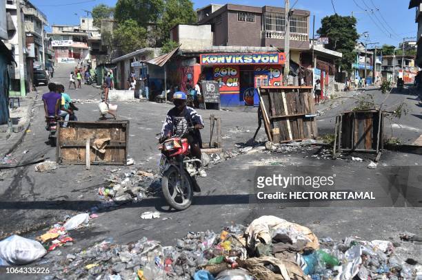 Man navigates his motorcycle past a barricade and strewn trash in Port-au-Prince, on November 22 amid anti-government protests in Port-au-Prince,...