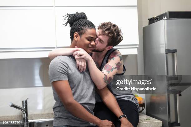 Loving gay man kissing his partner hugging him while sitting on kitchen counter