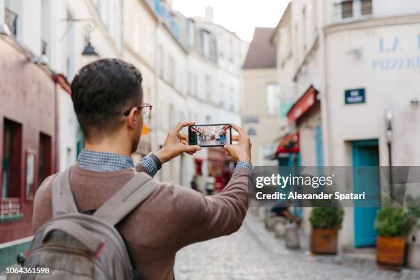 rear view of a young man taking pictures of montmartre street with smart phone, paris, france - taken on mobile device stock pictures, royalty-free photos & images