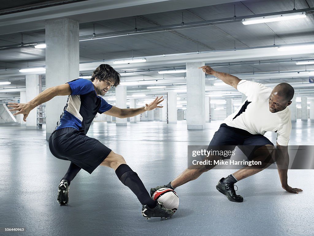 Two Athletic Males Playing Football In A Carpark