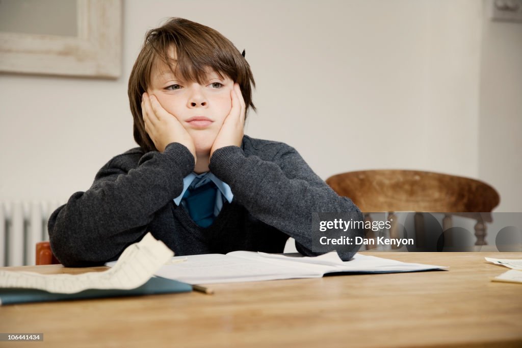 BOY SITTING AT TABLE WITH HOMEWORK LOKKING SAD