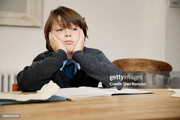 boy sitting at table with homework lokking sad - homework table stock pictures, royalty-free photos & images