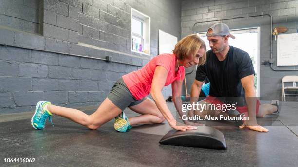 de aantrekkelijke senior, 55-jaar-oud, actieve latino vrouw doen uitrekkende training onder de begeleiding van de jonge mannelijke coach. - 55 years old white man active stockfoto's en -beelden