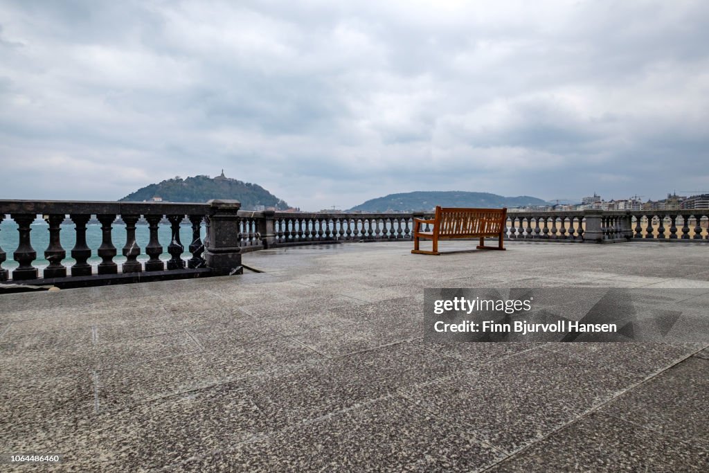 Viewpoint at the beach of San Sebastian Spain. Concrete fence and a red bench. City in the background