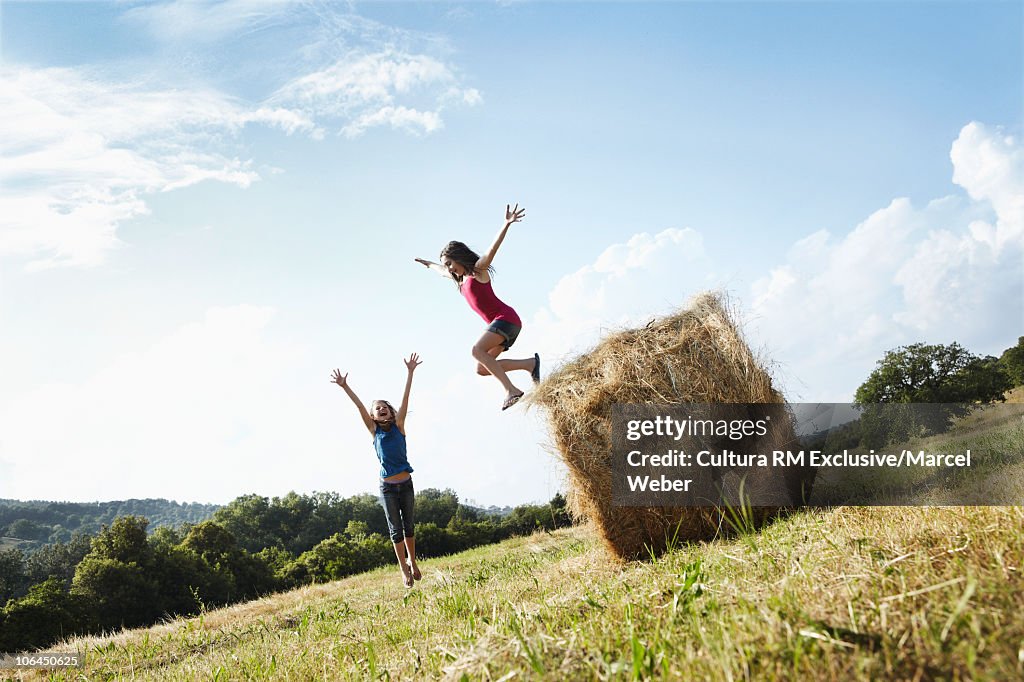 Girls jumping off bale of hay