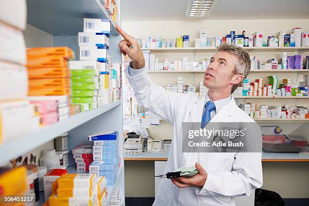 pharmacist looking at shelf of pills - uk pharmacy shop stock pictures, royalty-free photos & images