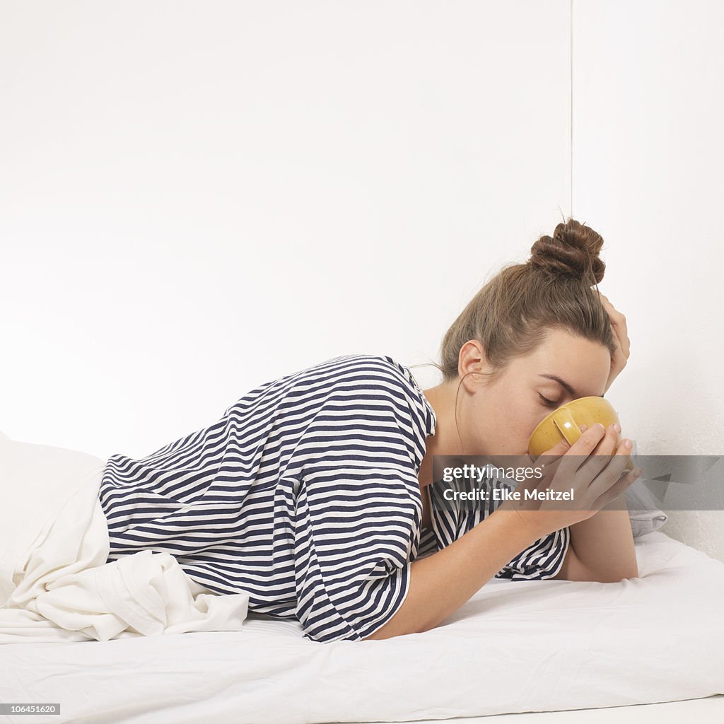 Woman in bed drinking from mug