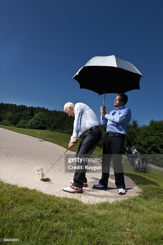 Caddy is holding a parasol over a golfer