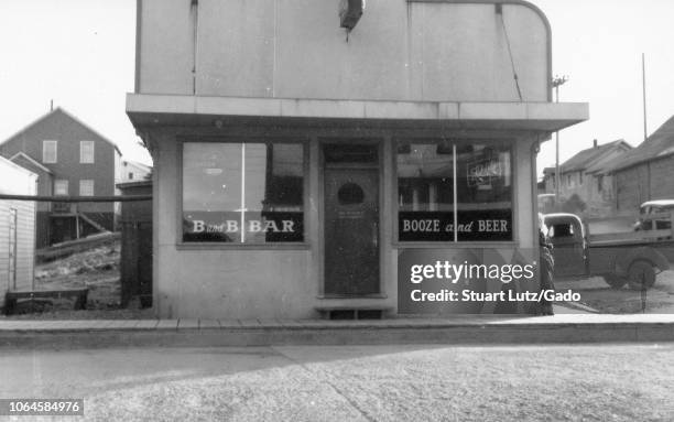 Black and white photograph of a small building with an Art Deco-era facade and text in the windows reading "B and B Bar" and "Booze and Beer, " with...