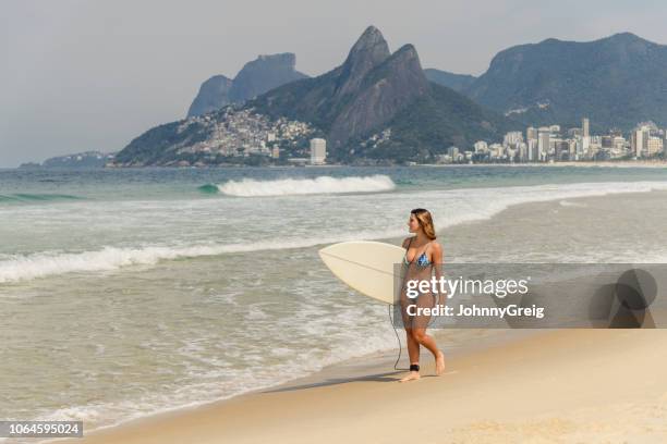 young woman carrying surfboard, ipanema beach - ipanema beach stock pictures, royalty-free photos & images