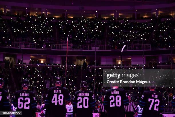 Players with their sticks raised and fans join in a moment of silence before the San Jose Sharks and Vancouver Canucks game at SAP Center on November...
