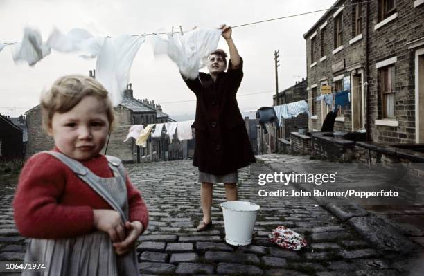 Woman strings her washing across the street paved with setts in Halifax, West Yorkshire in 1965.