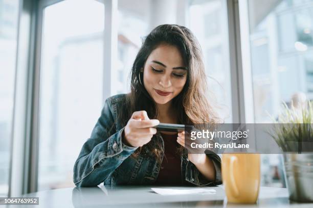 hermosa joven depositar cheque con smartphone - electronic banking fotografías e imágenes de stock