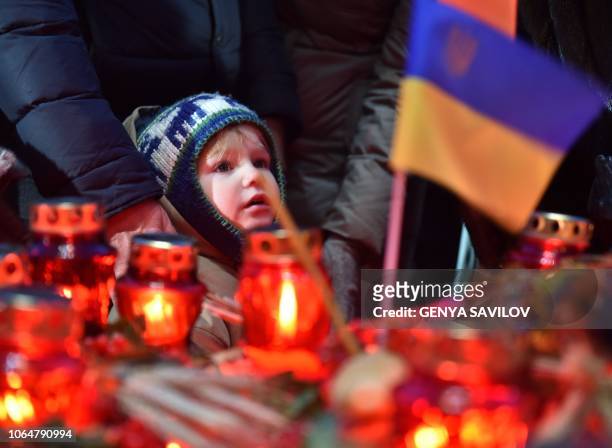 Child looks as people laying symbolic sheaves of wheat and lit candles during a commemoration ceremony at a monument to victims of the Holodomor...