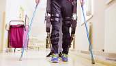 Legs of invalid in robotic exoskeleton walking through the corridor