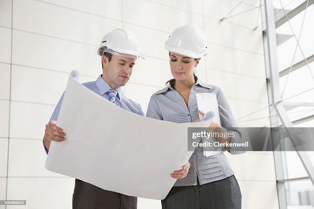 Male and female architects looking at blue print