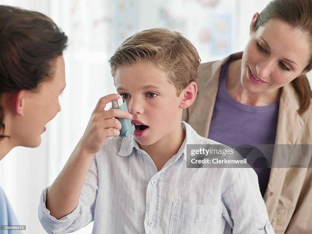 Mother watching nurse help boy (10-11) with an asthma inhaler