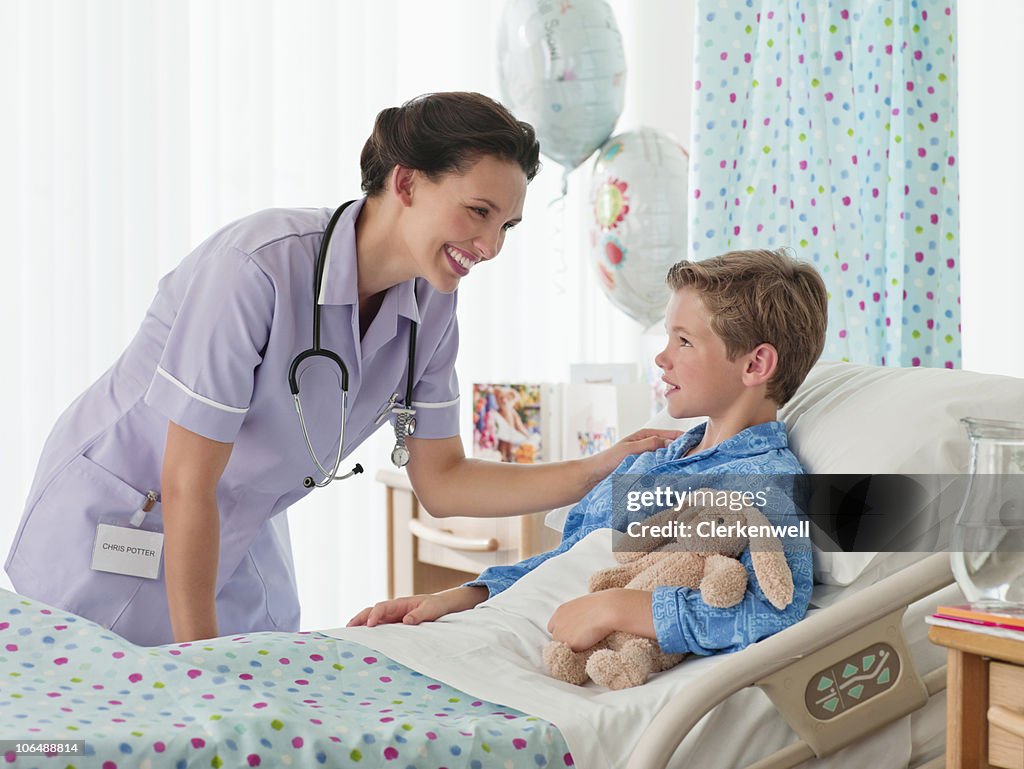 Affectionate happy nurse looking at boy (10-11) in hospital bed