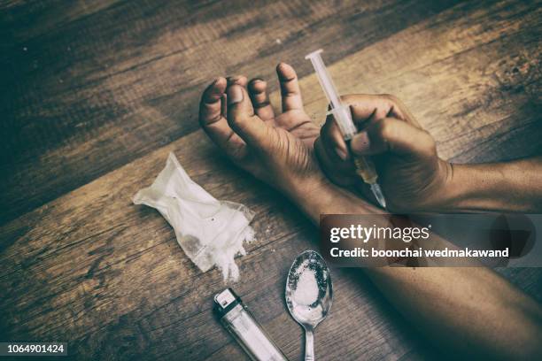 unconscious drug addict hands lying on grungy concrete floor with pills, syringe, cooked heroine. dangers of drug addict and abuse concept. international day against drug abuse. - injecting heroin stock pictures, royalty-free photos & images