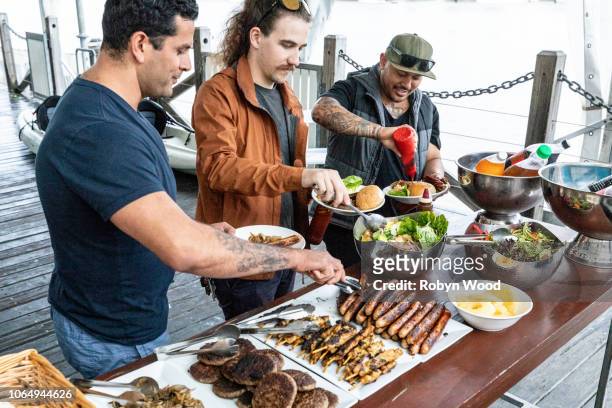 trio of men serves themselves food from bbq buffet. - australian bbq stockfoto's en -beelden