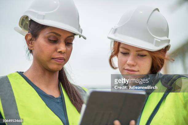 två unga kvinnor ingenjörer på plats kontrollera detaljer på digitala tablett - builder apprenticeship bildbanksfoton och bilder