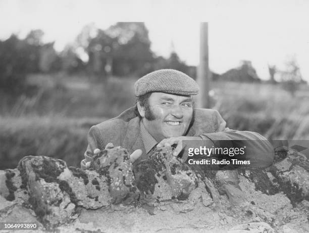 Comedian Les Dawson peering from behind a stone wall during the filming of the television show 'The Dawson Watch' in Ross-on-Wye, August 1980.