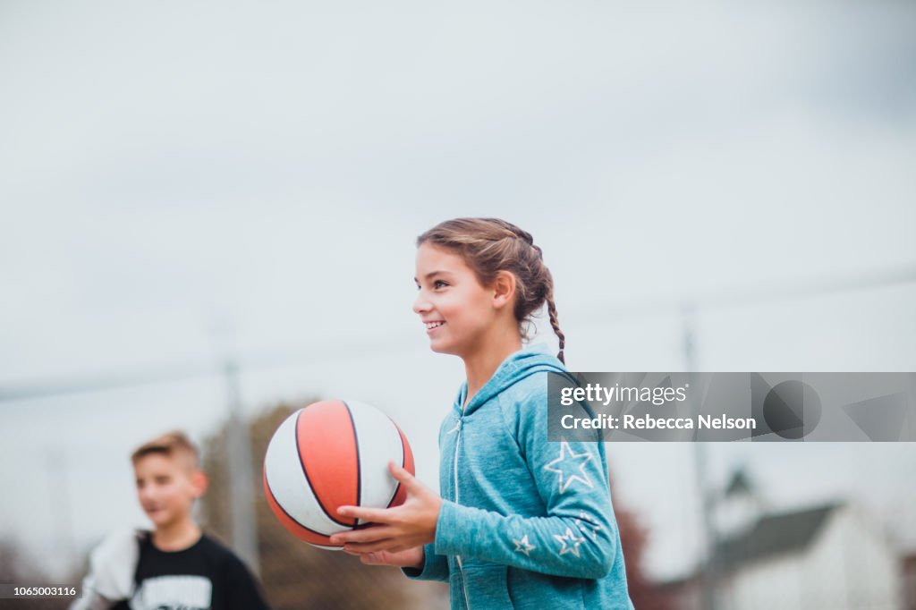 Pre-teen boy and girl playing basketball on the playground
